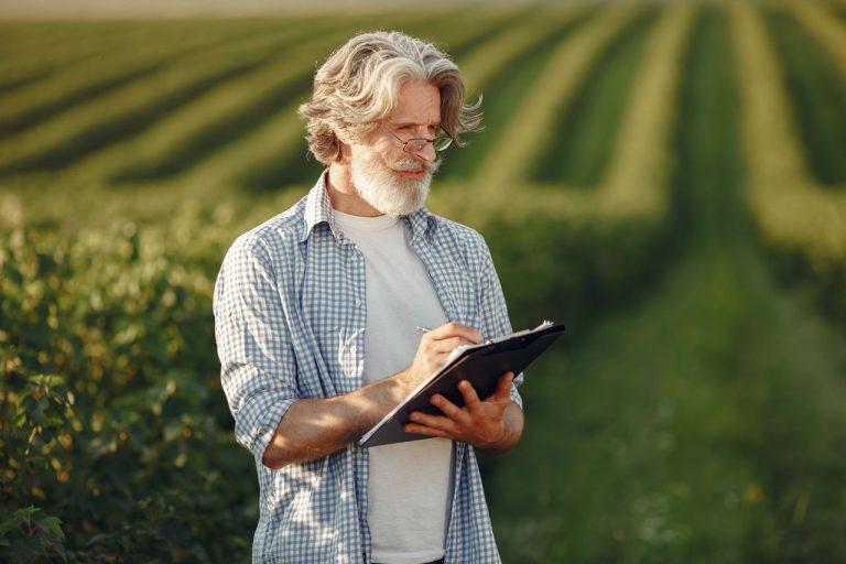 O que muda no planejamento rural com as orientações da Embrapa para o El Niño Agricultor de pé em uma lavoura verde, fazendo anotações em uma prancheta.