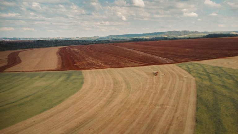 Vista aérea de extensas áreas cultivadas, com um trator trabalhando no campo.